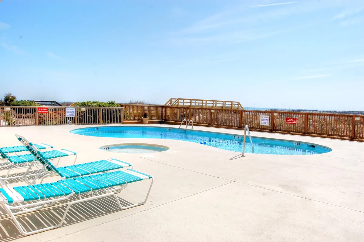 This image captures an inviting exterior view of the oceanfront outdoor pool and hot tub, surrounded by lounge chairs and with a panoramic ocean view in the background. Guests are enjoying swimming, sunbathing, and relaxing by the water, creating a vibrant yet tranquil atmosphere reflecting resort-style leisure.