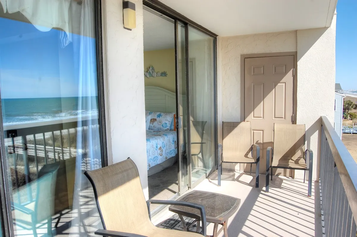 The image features a private balcony with two chairs and a small table, all overlooking a stunning ocean view. The tranquil setting is perfect for sipping morning coffee, watching the sunrise, or unwinding as the waves roll in.