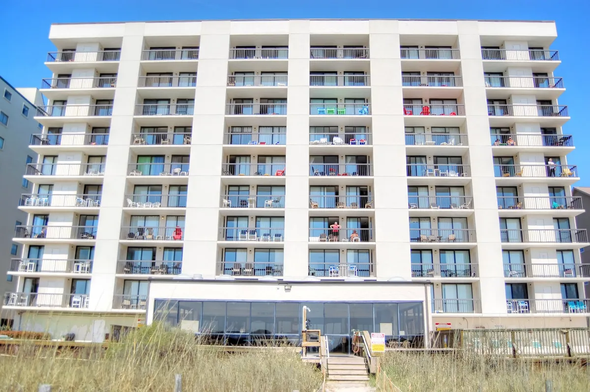 This image highlights balconies outfitted with chairs, a large glass entrance, and a sandy path leading directly to the beach. The view connects the property to the beach environment, evoking the experience of enjoying ocean vistas and easy beach access.