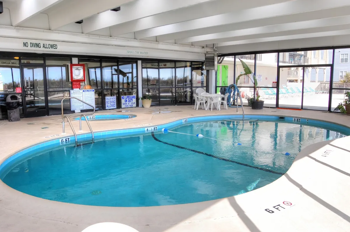 This photo showcases a bright and welcoming indoor swimming pool with lounge chairs and large windows, creating a relaxed atmosphere for swimming, gathering with friends, or unwinding after a day at the beach.