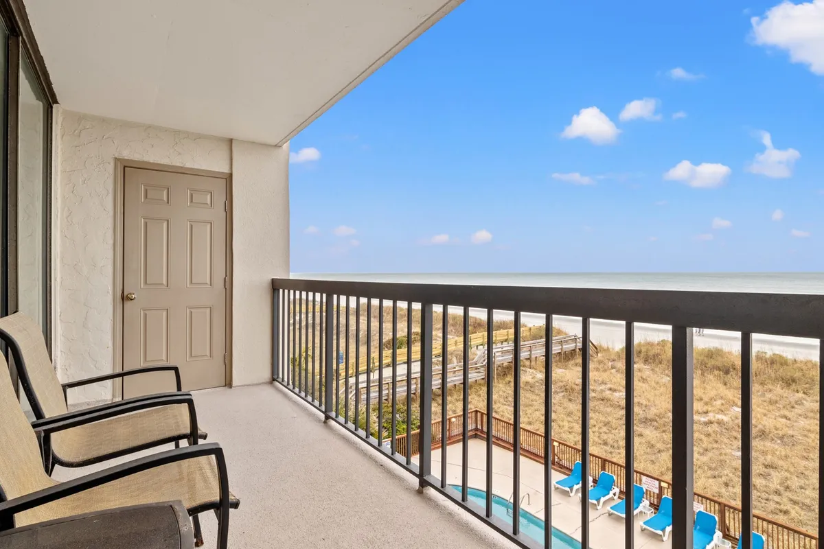 This image features a private balcony with a railing overlooking a beautiful beach and the pool area below. The serene scene suggests early morning or evening, with gentle light and calm water. The setting invites guests to relax on the balcony, enjoy ocean breezes, or watch the sunrise over the Atlantic.