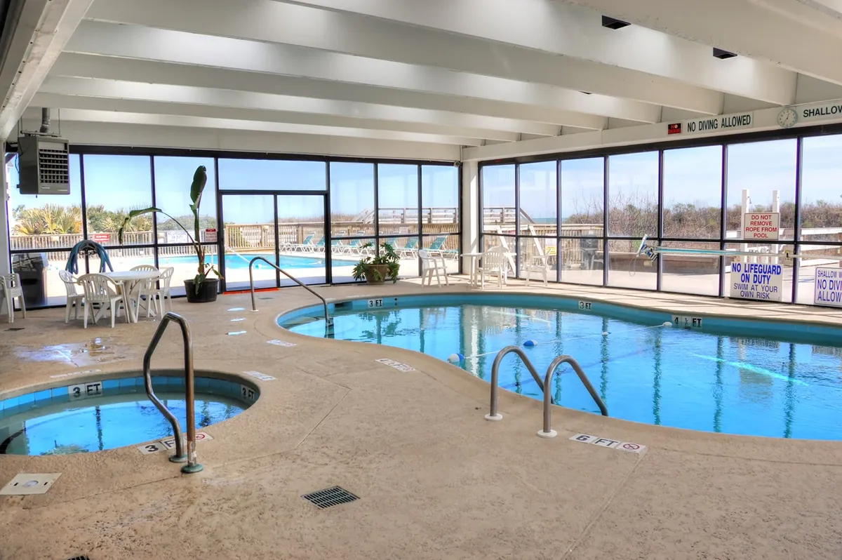 An indoor swimming pool and jacuzzi are featured in this calm and refreshing scene, with large windows letting in natural light and a seating area for guests to relax. The setting promises year-round enjoyment, whether for a morning swim or a soothing soak.