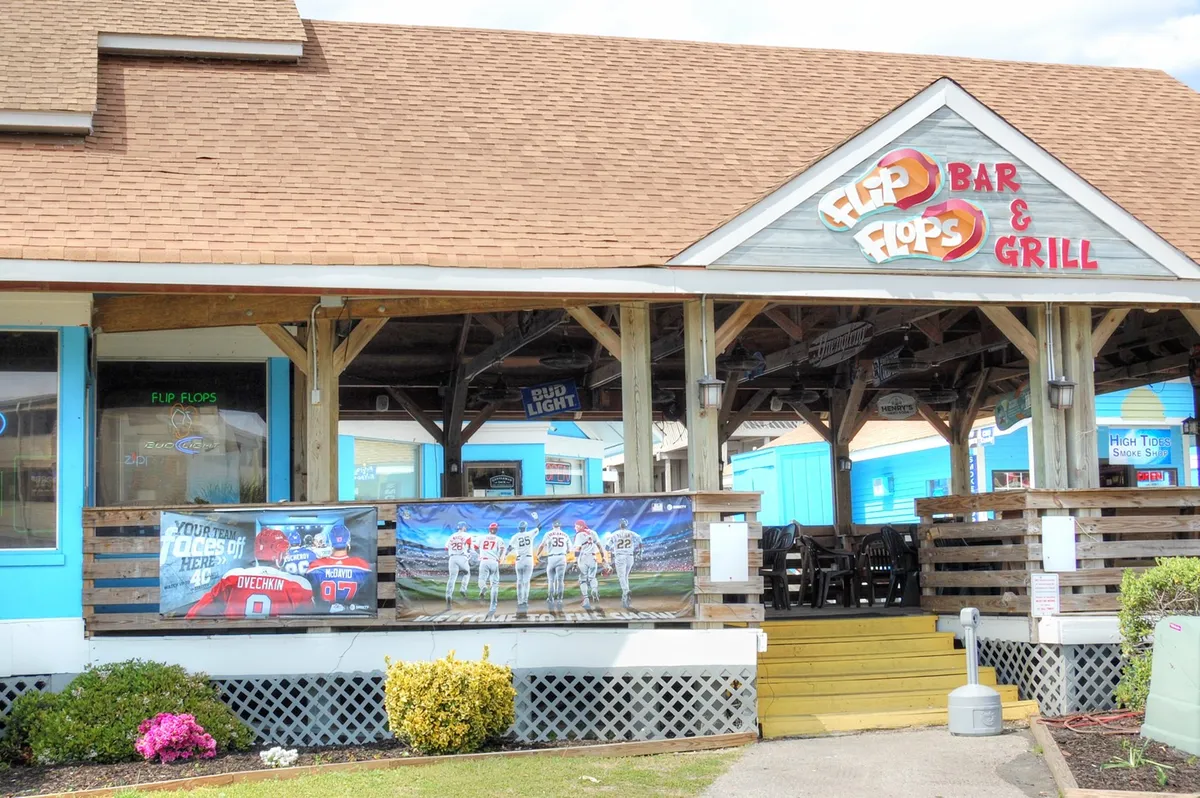 This exterior image features an inviting bar and grill sign, sports-themed artwork, and an outdoor seating area. The mood is casual and energetic, suggesting a lively spot for dining and socializing.
