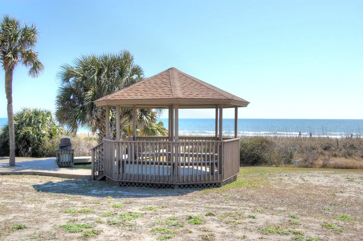 A serene outdoor gazebo facing the ocean, surrounded by palm trees and open skies. The setting is perfect for relaxation, picnics, or quiet contemplation, with beautiful water views and space for community gatherings.